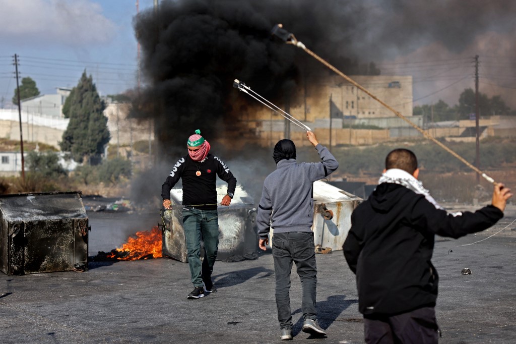 Palestinians use slingshots to throw stones towards Israeli soldiers during a demonstration in Ramallah, in the occupied West Bank on October 18, 2023, following a strike which ripped through a Gaza hospital compound killing hundreds the day before. Thousands rallied across the Arab world on October 18 to protest the deaths of hundreds of people in a strike on a Gaza hospital they blame on Israel, despite its denials. (Photo by Thomas COEX / AFP)||||||